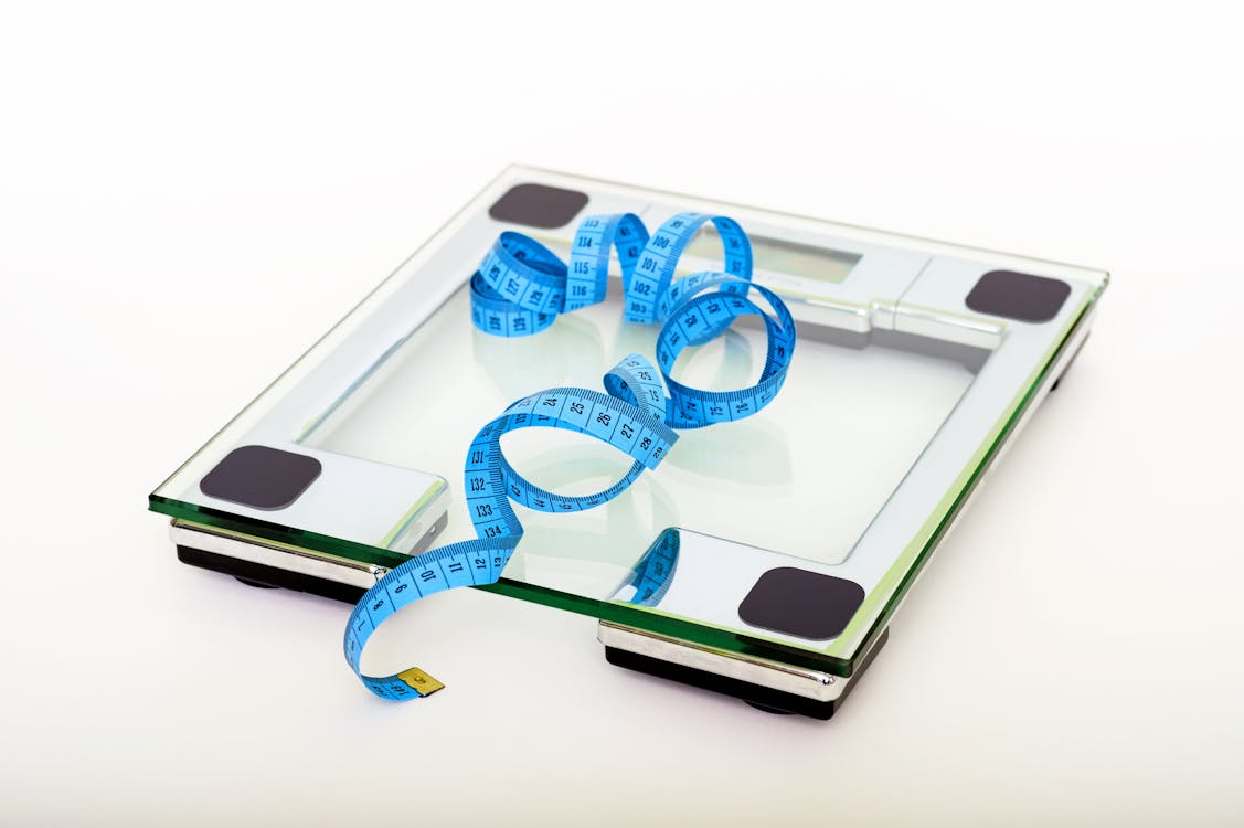 Free A digital glass weighing scale with a blue measuring tape, symbolizing weight management. Stock Photo